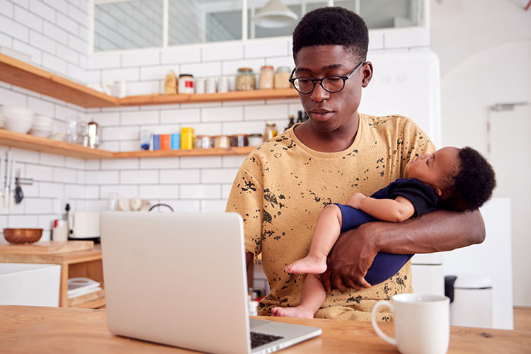 멀티 태스킹 아버지는 잠자는 아기 아들을 안고 부엌에서 노트북 컴퓨터에서 작동